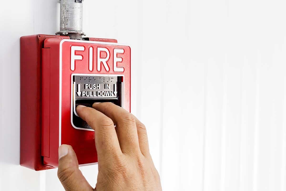 Hand pulling a red fire alarm pull station
